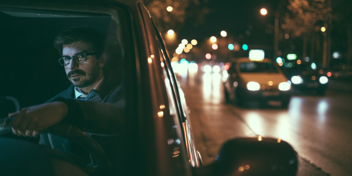 Man sitting in car on side of street at night